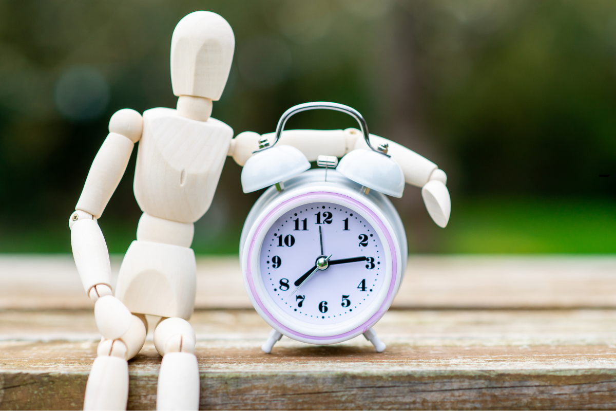 Un mannequin en bois pose son bras sur un réveil matin, illustrant le concept des rythmes circadiens et de l’horloge biologique.